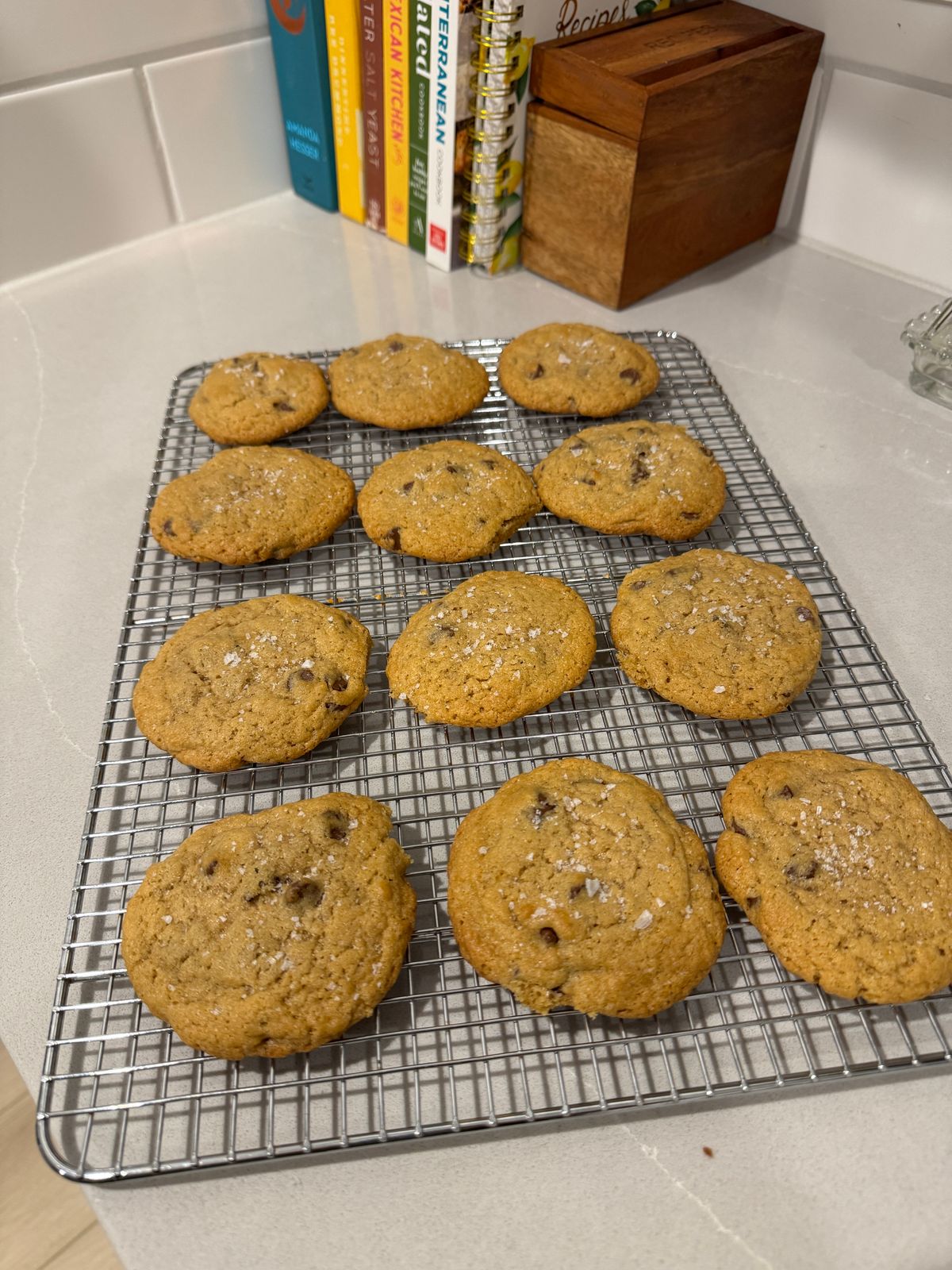A tray of large rustic chocolate chip cookies cooling on a wire rack, flecked with sea salt.